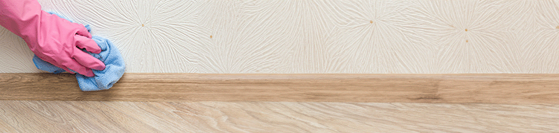 gloved hand cleaning a baseboard