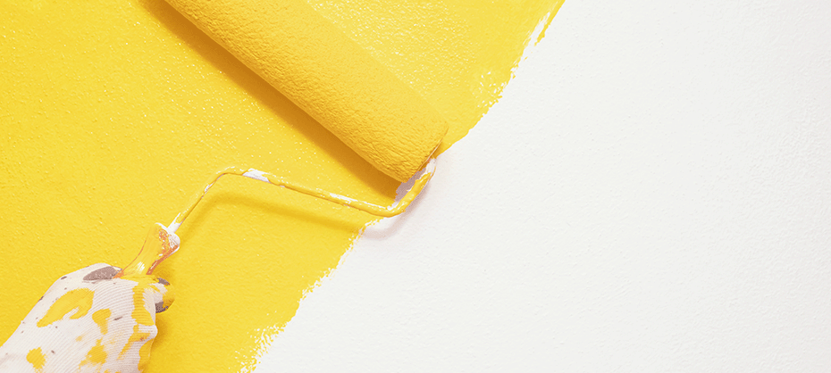 gloved hand painting a wall yellow